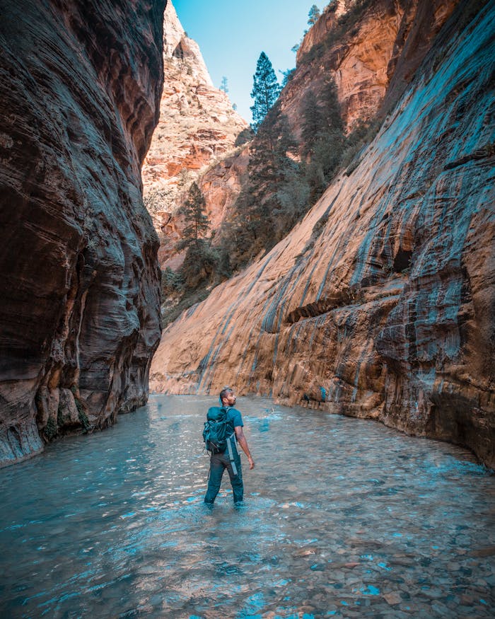 Hiker ventures into the scenic Narrows of Zion National Park's slot canyon. Tranquil wilderness.